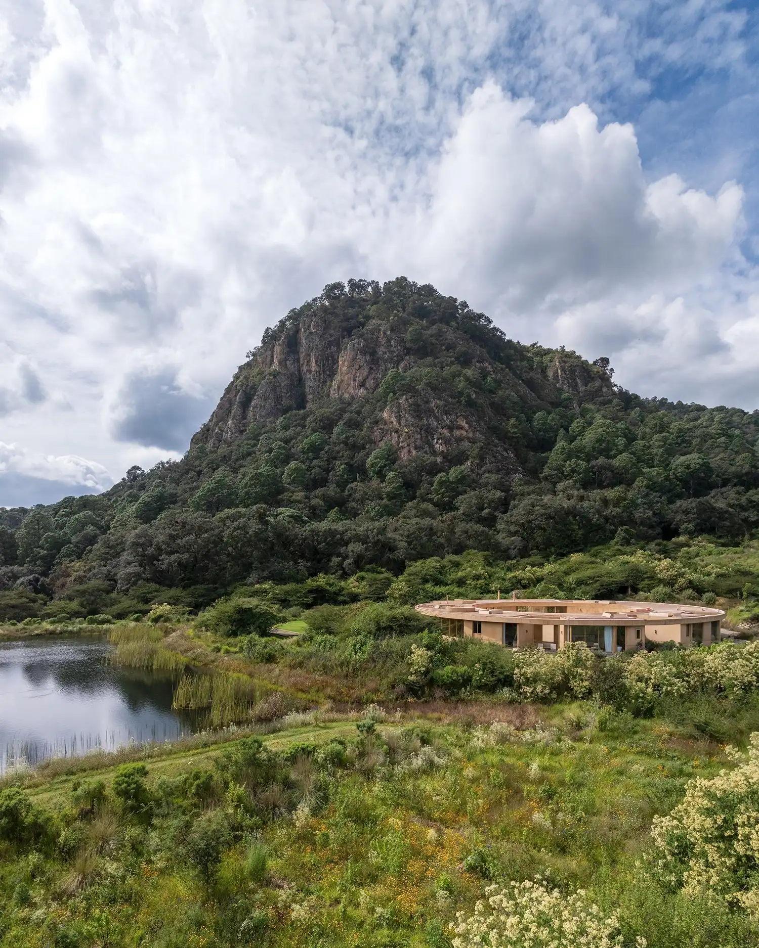 Aerial-style view of the circular House 720 Degrees in a green valley next to a lake and mountain.
