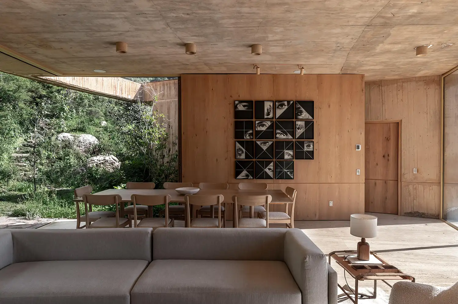 Dining area with a long wooden table and chairs in a room with a concrete ceiling and wood-paneled walls.