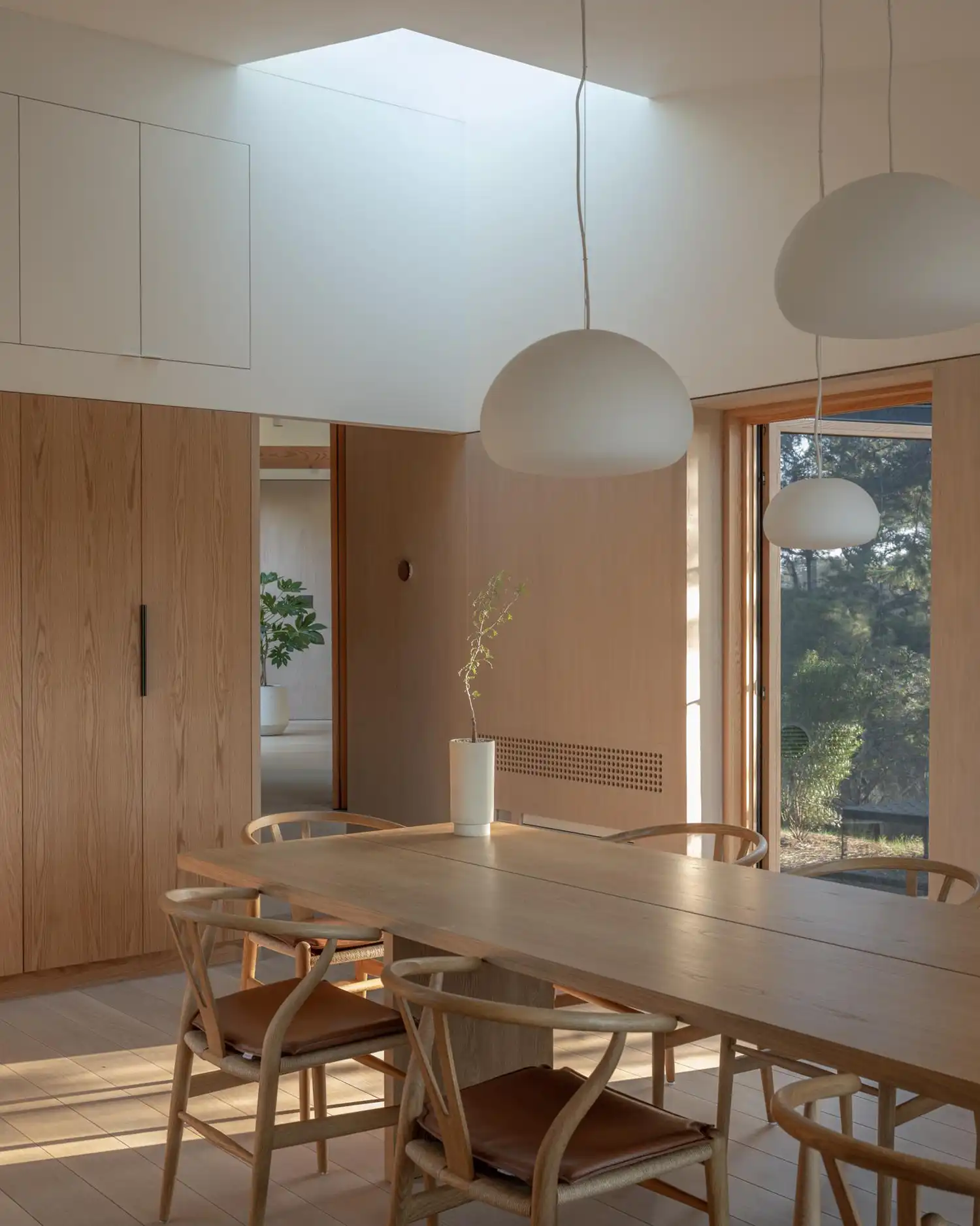 Minimalist dining room with light wood furniture, pendant lights, and a skylight.