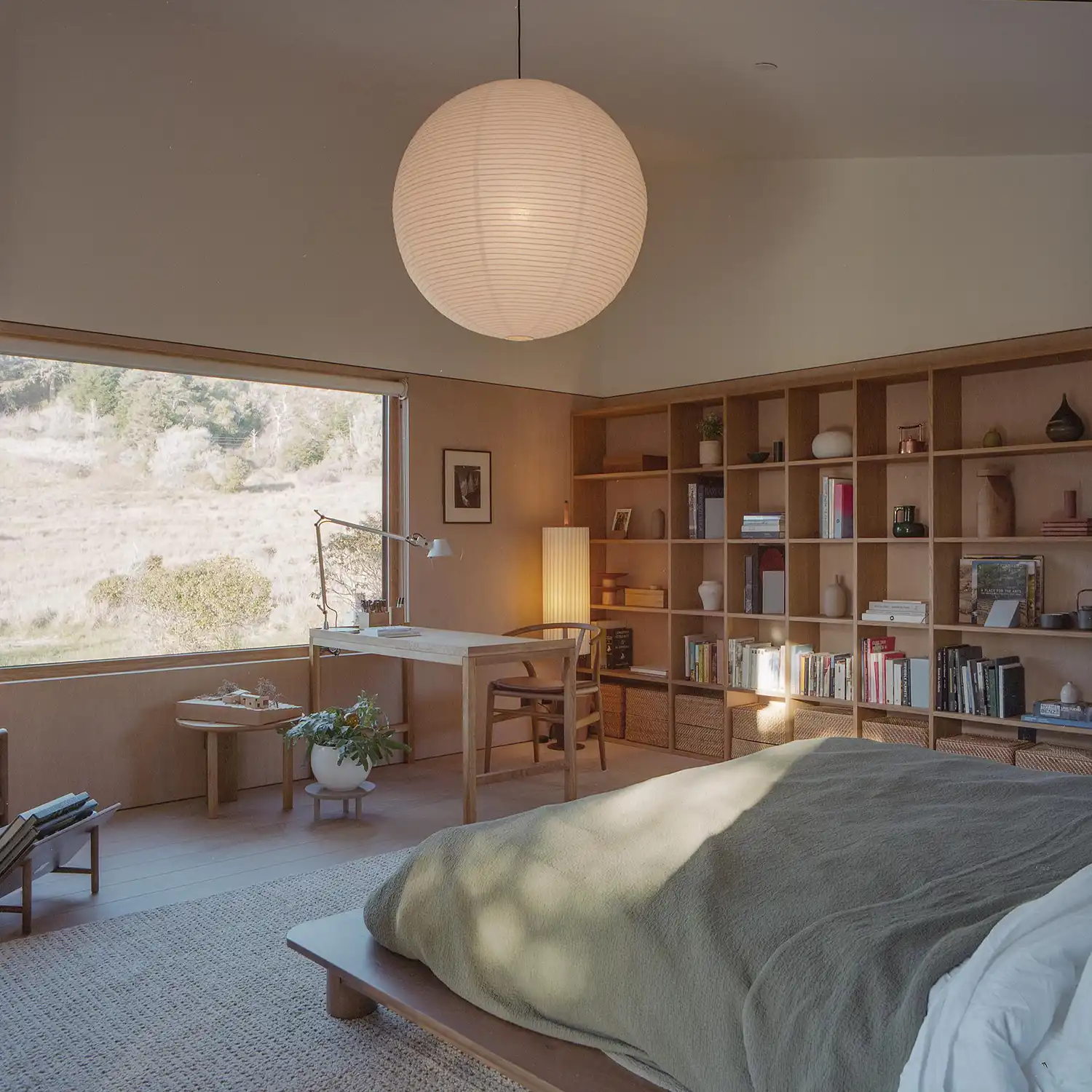 Airy bedroom with a large panoramic window overlooking a meadow and built-in bookshelves.