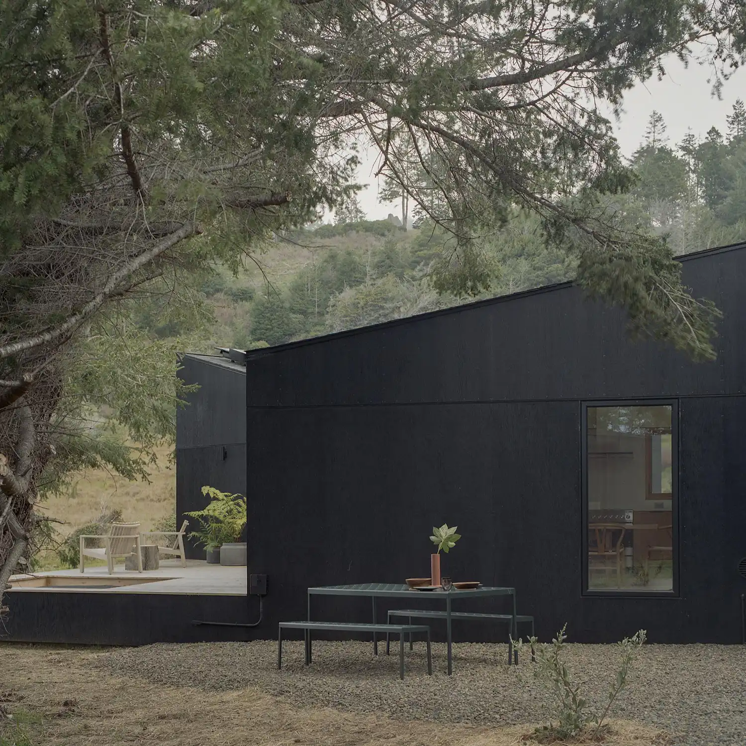Outdoor dining area with dark metal furniture next to a black timber wall under tree branches.