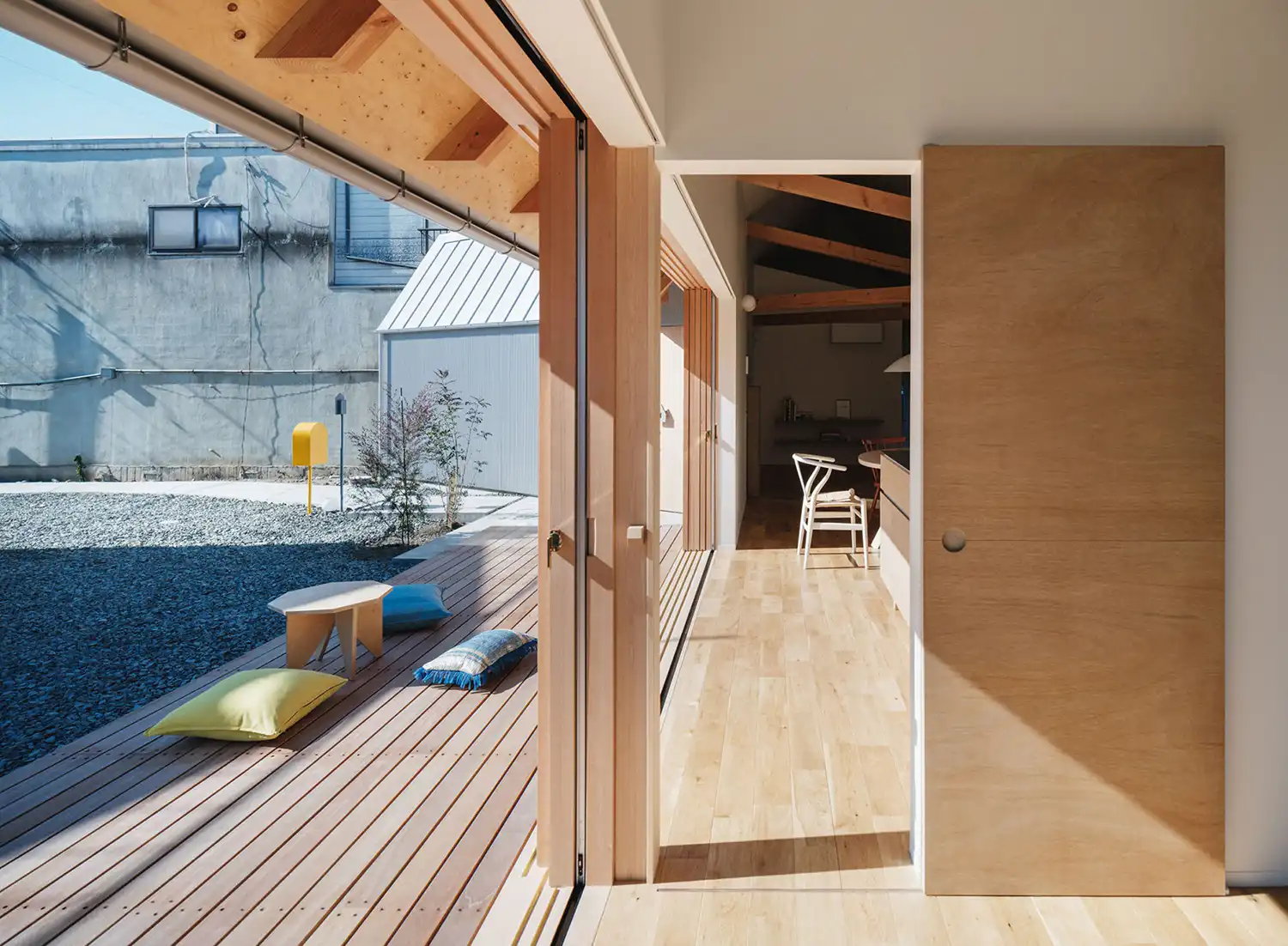 Interior perspective looking out from a wooden doorway toward a gravel courtyard and gabled outbuilding.