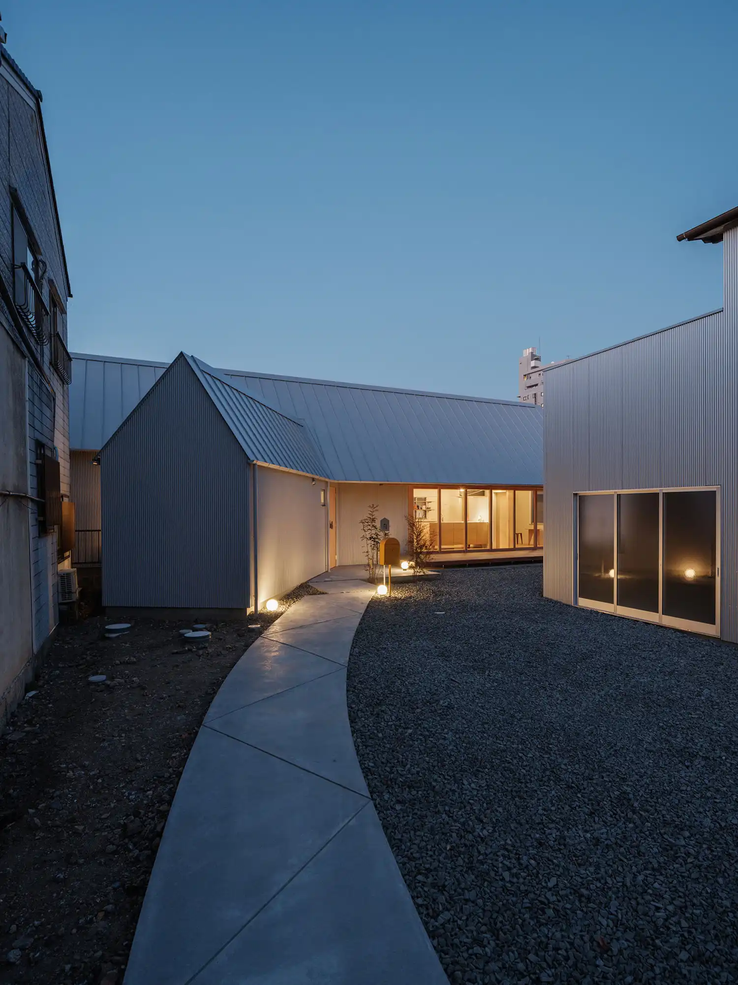 Night view of the concrete approach and illuminated volumes of the Kaleidoscape House in Tajimi.