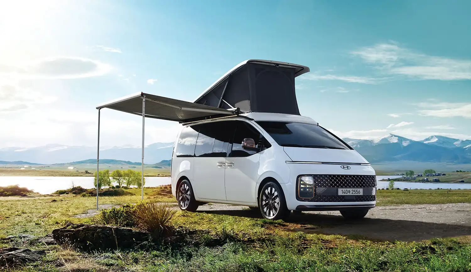 Front three-quarter view of the white Hyundai STARIA Camper with pop-up roof against a mountain backdrop.