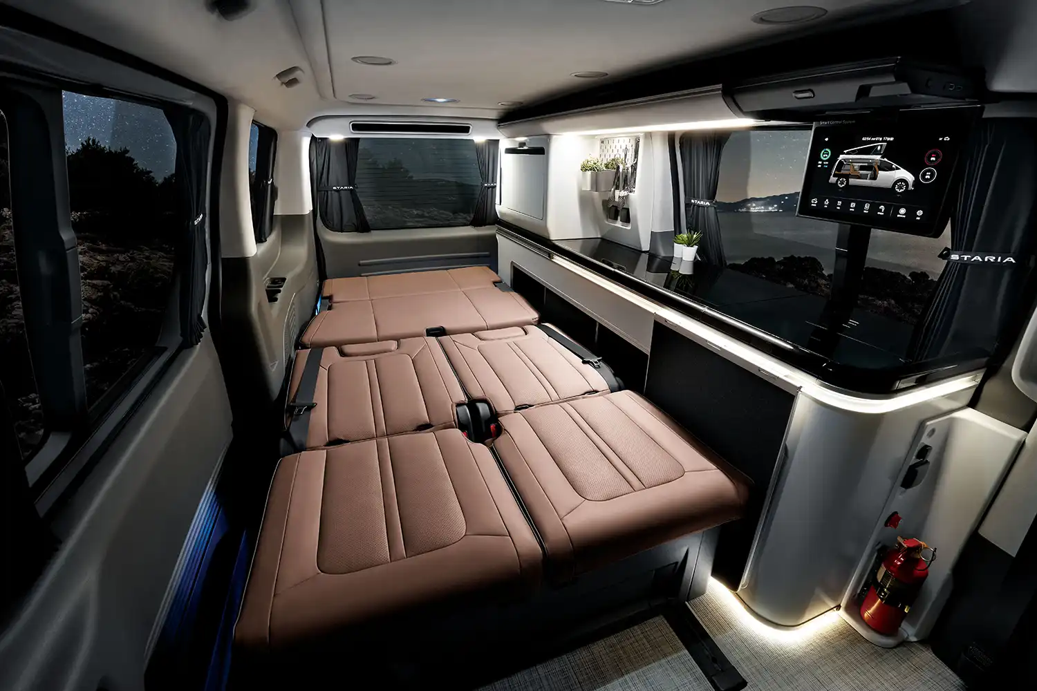Wide interior shot of the STARIA Camper with seats folded into a flat bed and smart control screen visible.