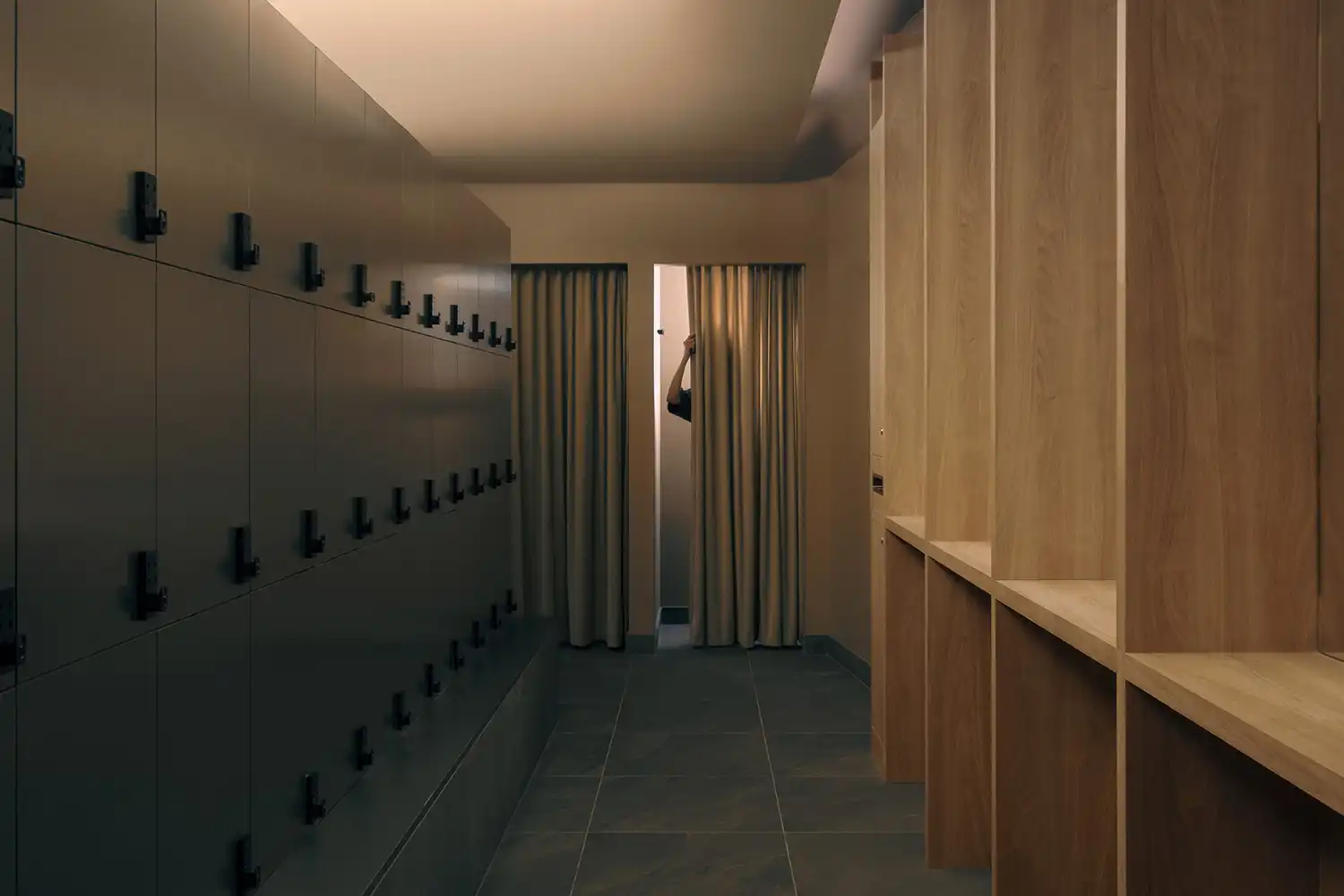A minimalist locker room with dark grey metal lockers on one side and light wood cabinetry on the other.