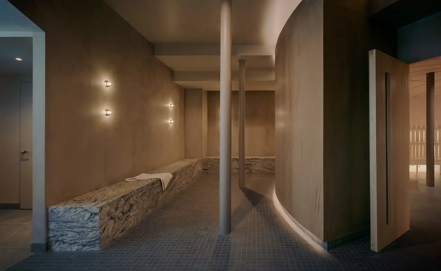 A dimly lit spa hallway with textured stone benches and warm orb wall lights.