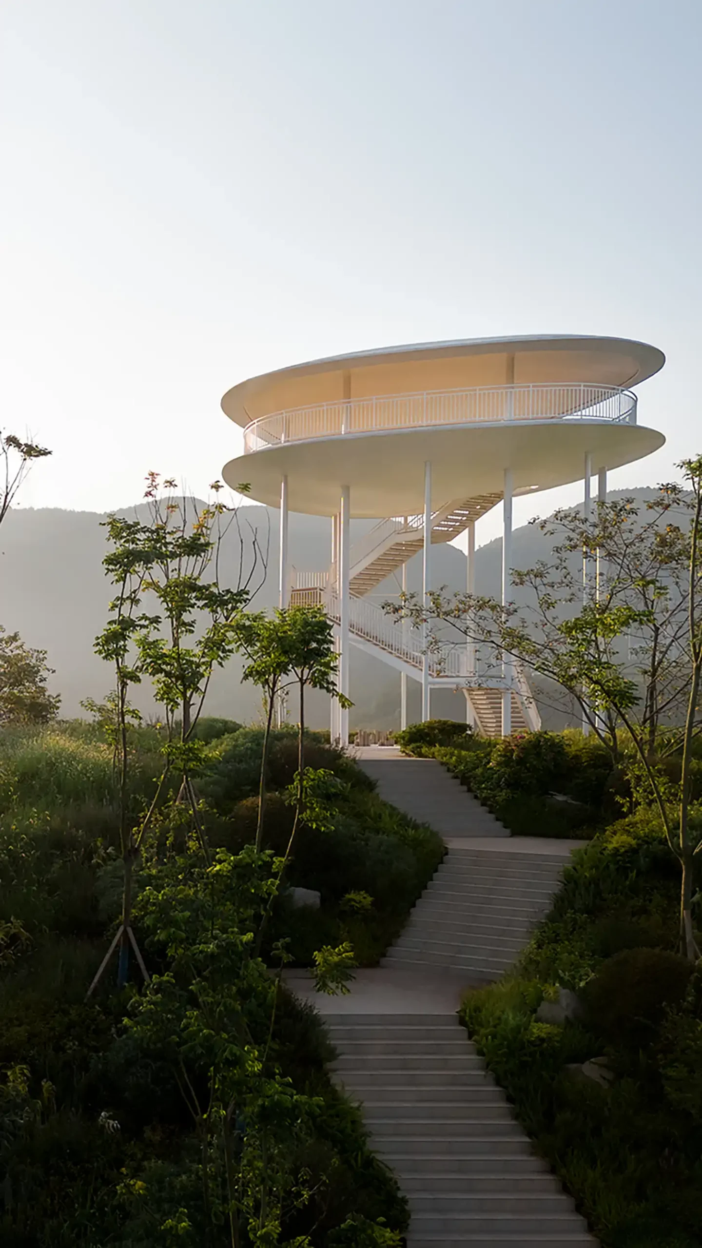 Stone staircase path leading up to the minimalist white Landscape Tower by gad in a lush green park.