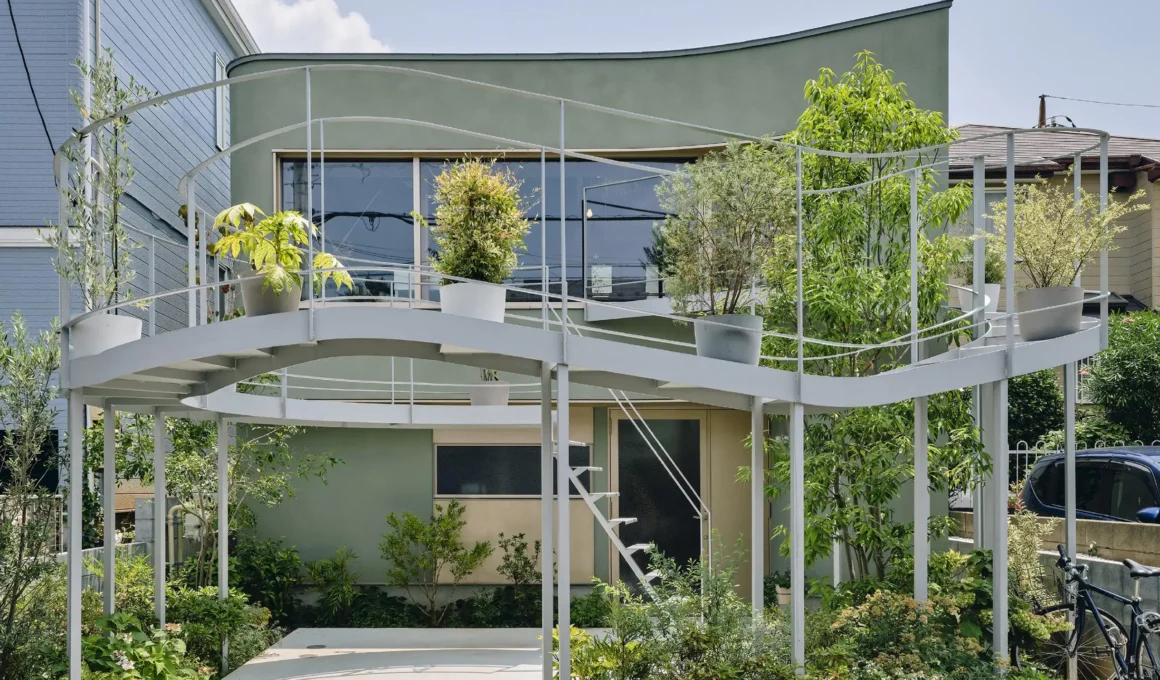A two-story modern house in Tokyo featuring a sage green façade and a prominent, elevated circular white metal terrace filled with potted plants.