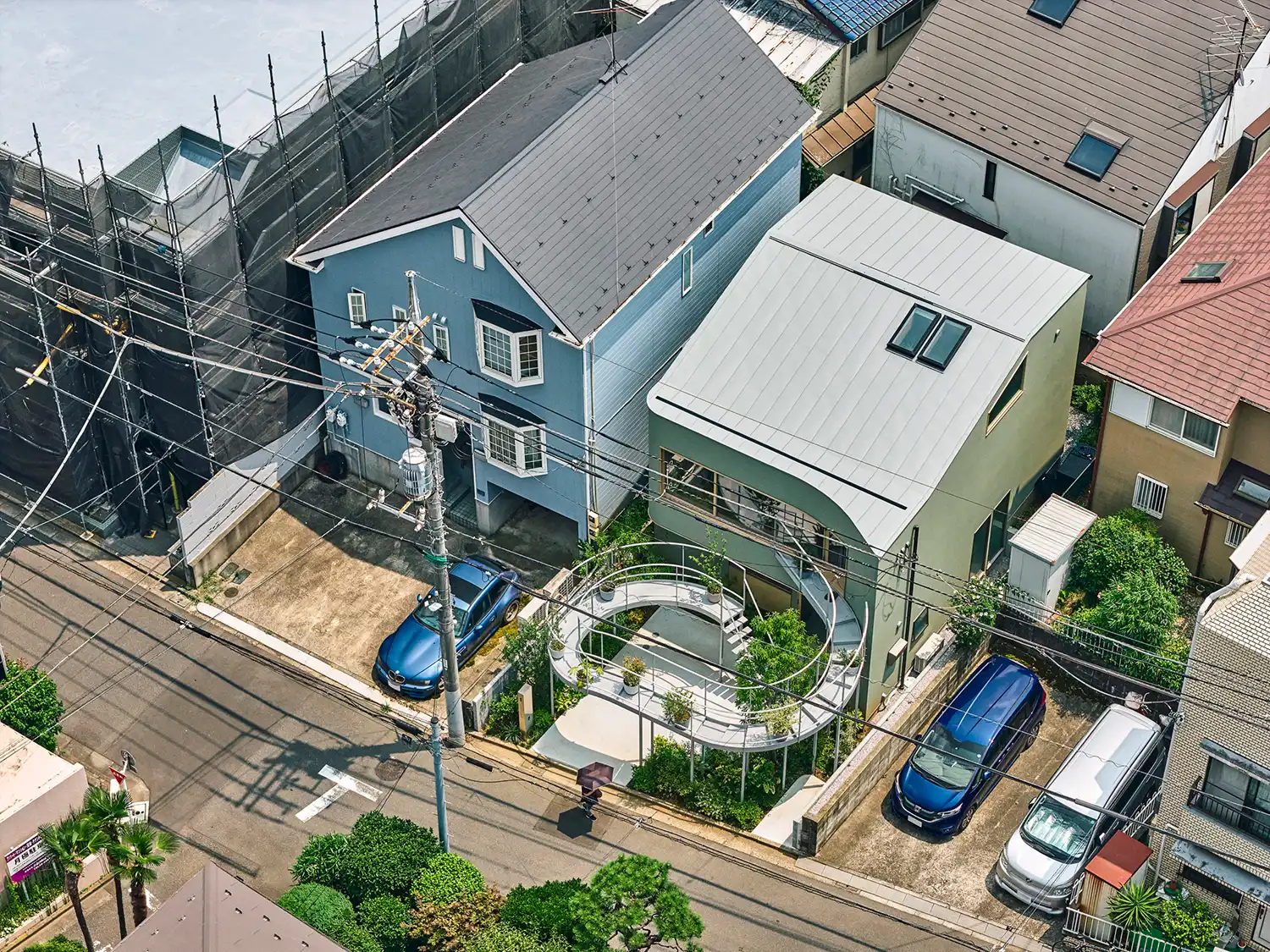 Aerial view of a dense Tokyo residential neighborhood showing the Kazari House with its unique curved terrace and slanted roof amidst traditional homes.
