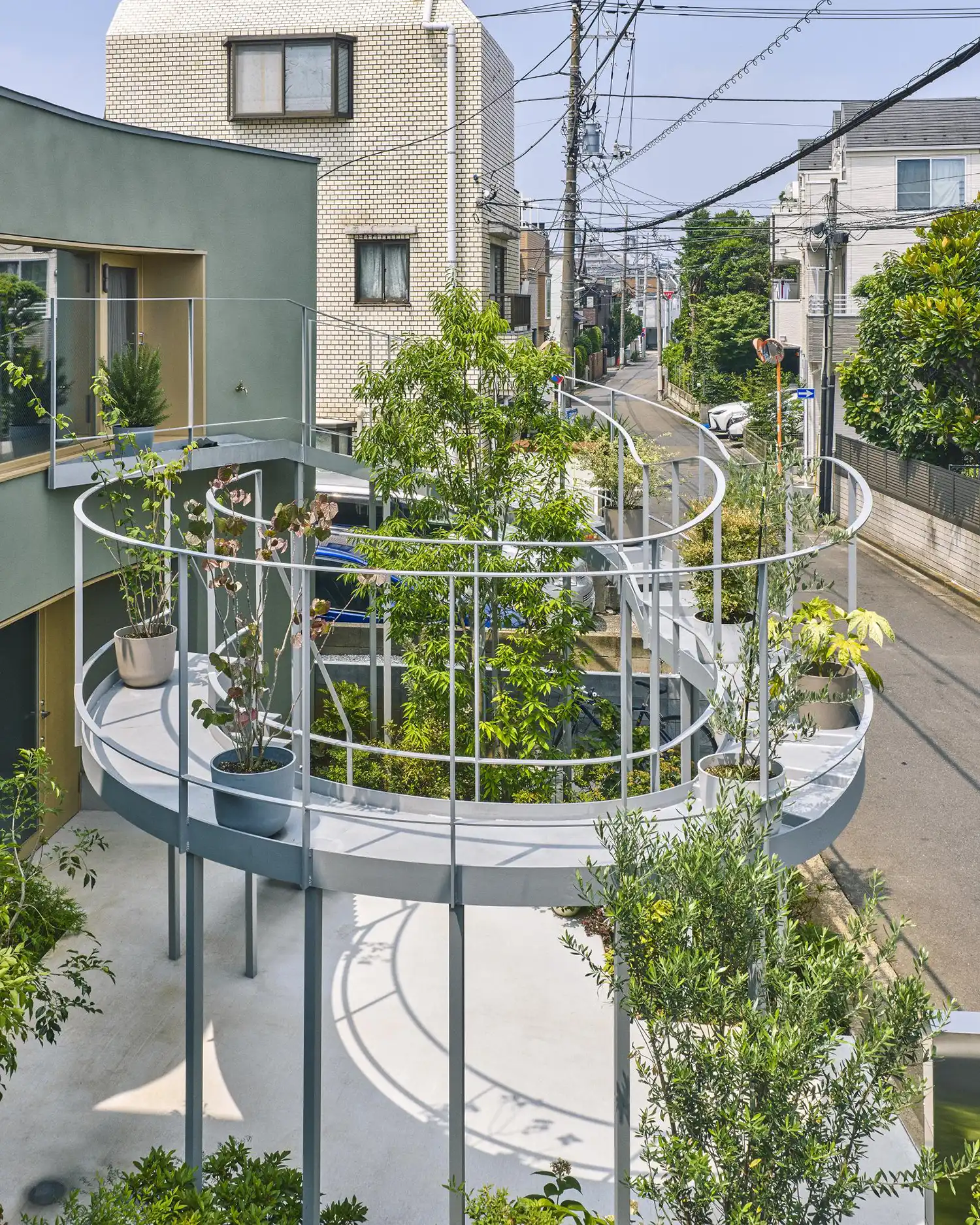 Close-up of a curved metal balcony walkway with several potted plants, overlooking a narrow Tokyo street.