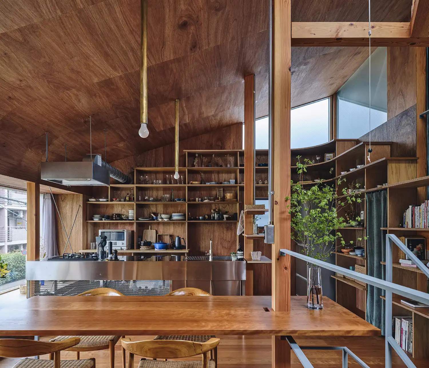 Modern Japanese interior with warm wood-paneled walls and ceilings, featuring a stainless steel kitchen island and built-in bookshelves.