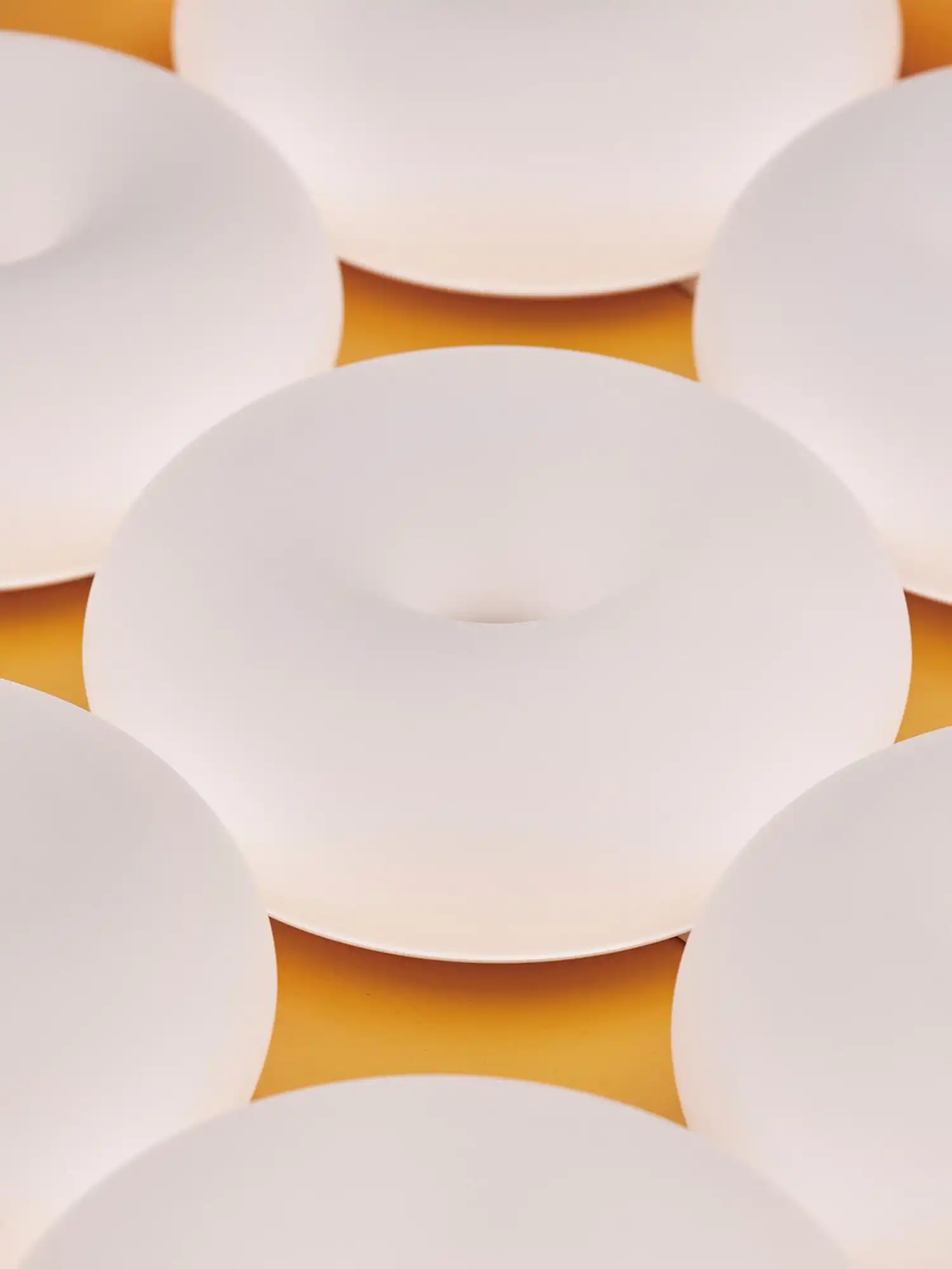 An array of circular matte white lamps viewed from a low angle, showcasing their sculptural "donut" geometry.
