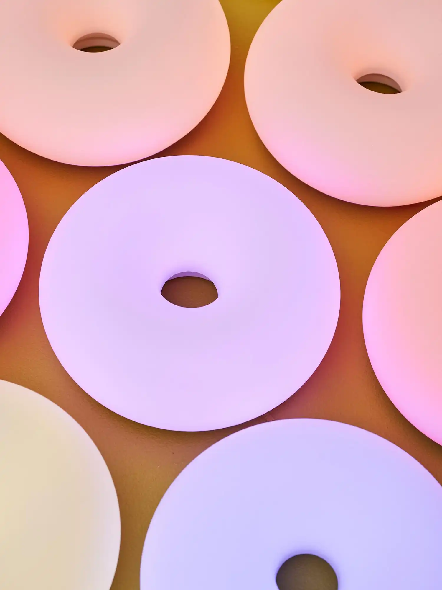 A top-down view of multiple VARMBLIXT donut lamps displaying various hues including lavender, soft pink, and pale yellow.