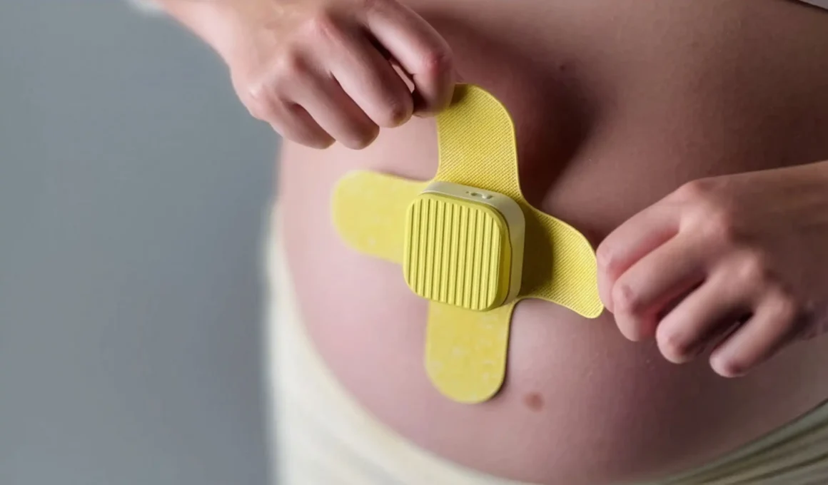 Close-up of hands applying the yellow MONI wearable device to a pregnant belly.