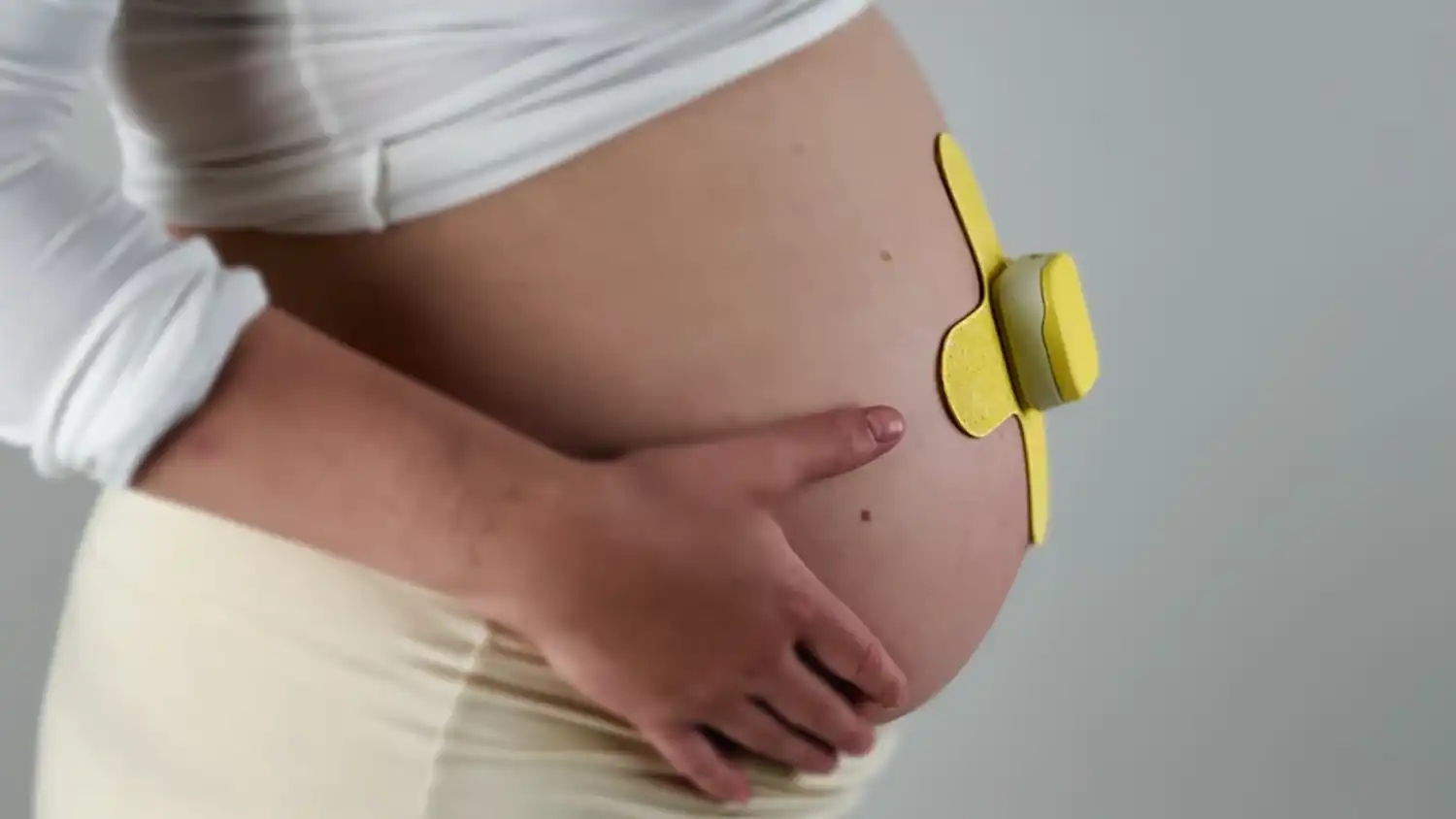 Profile view of a pregnant woman wearing the yellow MONI monitor.