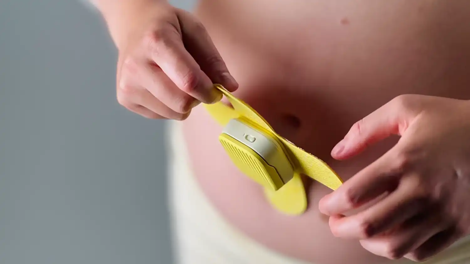 Perspective view of the MONI device being held against a pregnant abdomen.