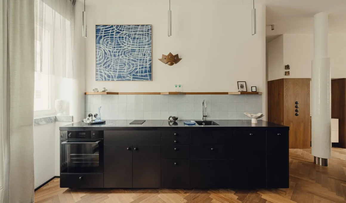 Minimalist black kitchen island against light blue tiles and herringbone floors.