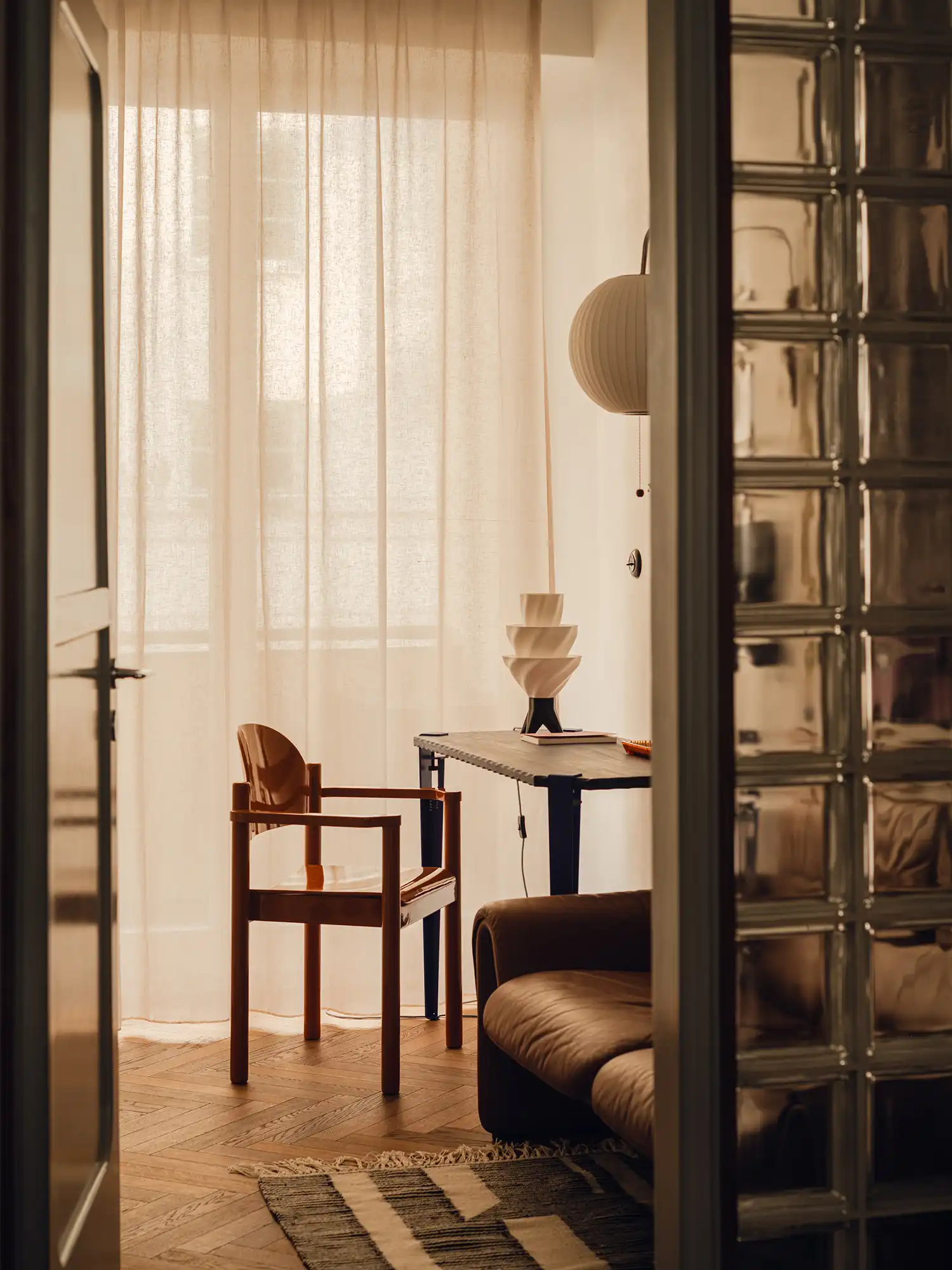 View through a doorway showing a wooden chair and a desk with a sculptural white lamp.