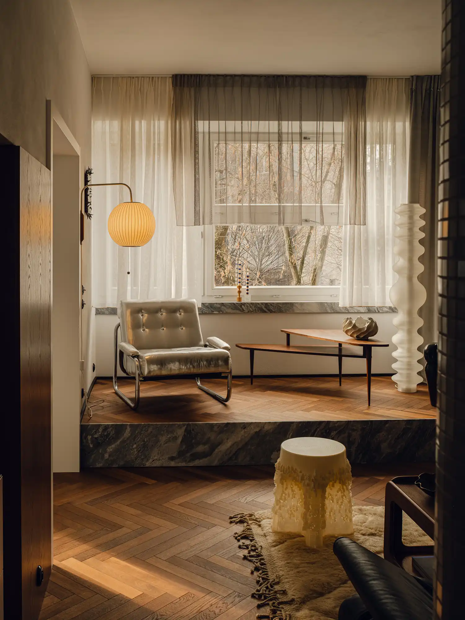 Raised marble platform in a living room with a silver armchair and wooden coffee tables.