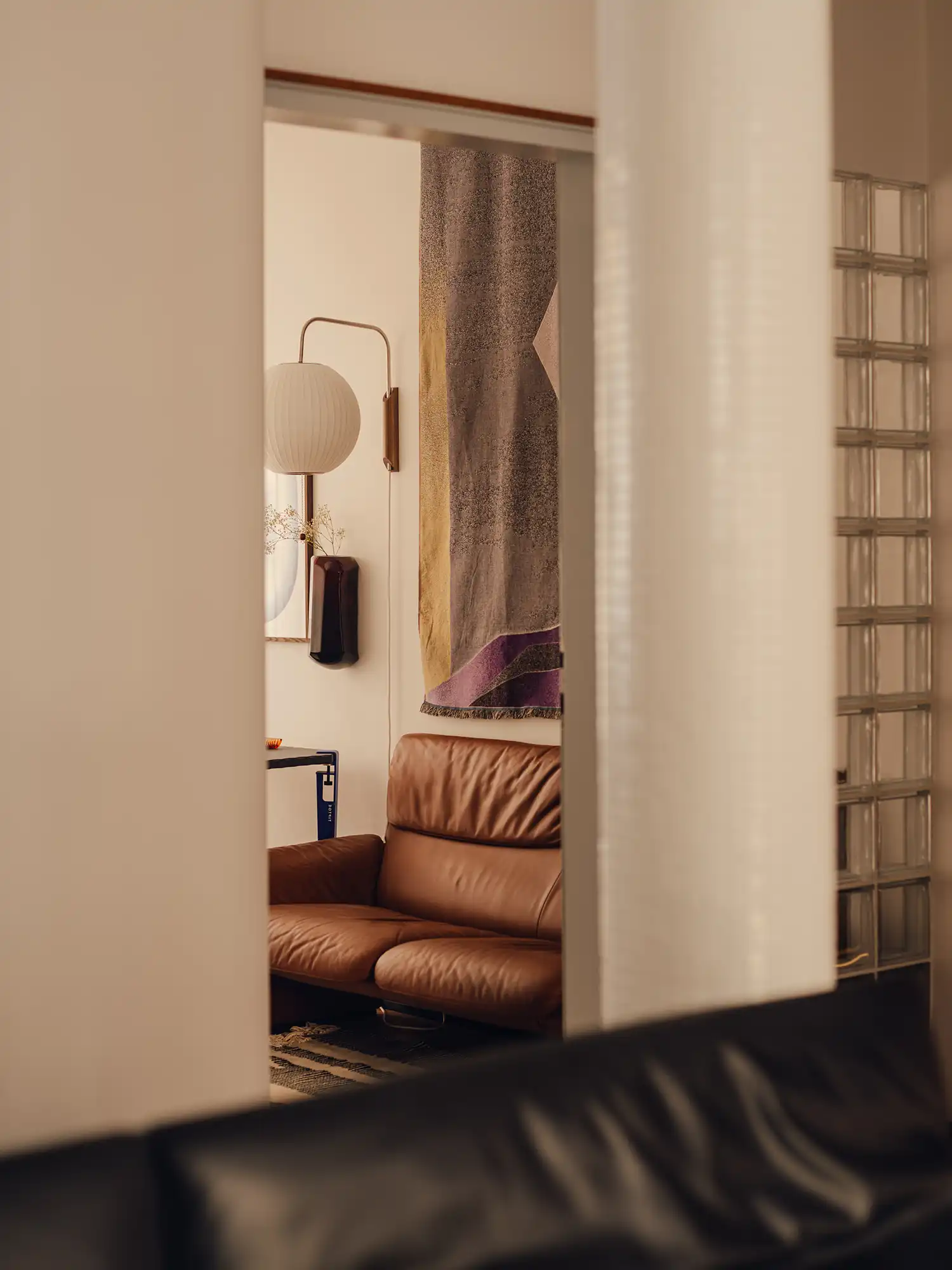 Detailed view of a brown leather sofa, paper wall lamp, and a geometric textile hanging.