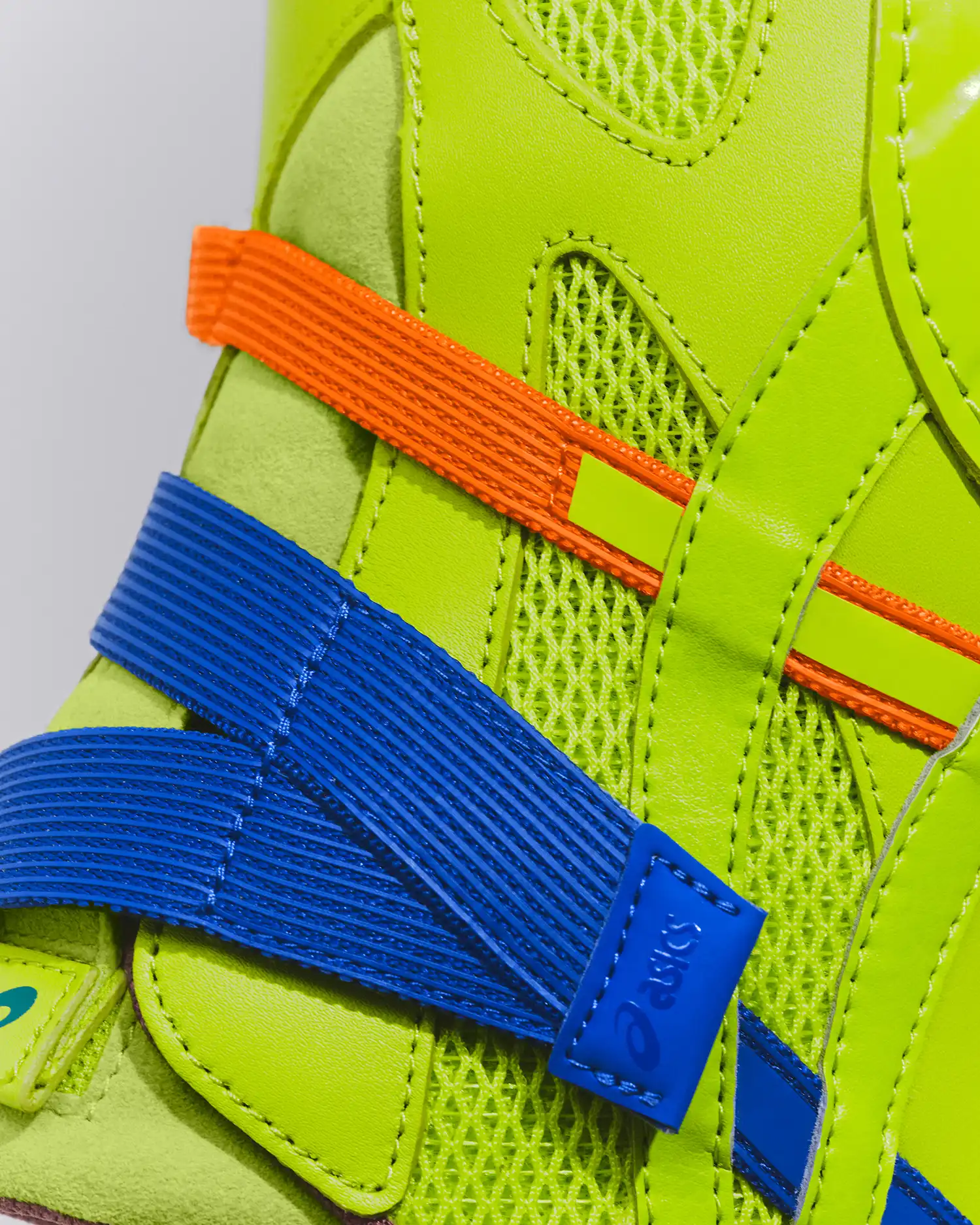 A macro close-up of the fluorescent green sneaker highlighting the vibrant blue and orange elastic bands integrated into the upper.