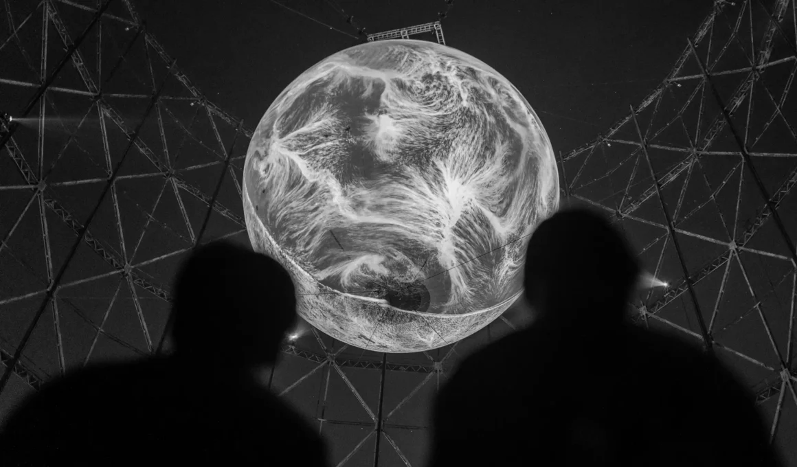 Silhouetted figures in the foreground looking up at a large spherical projection of swirling white energy patterns.