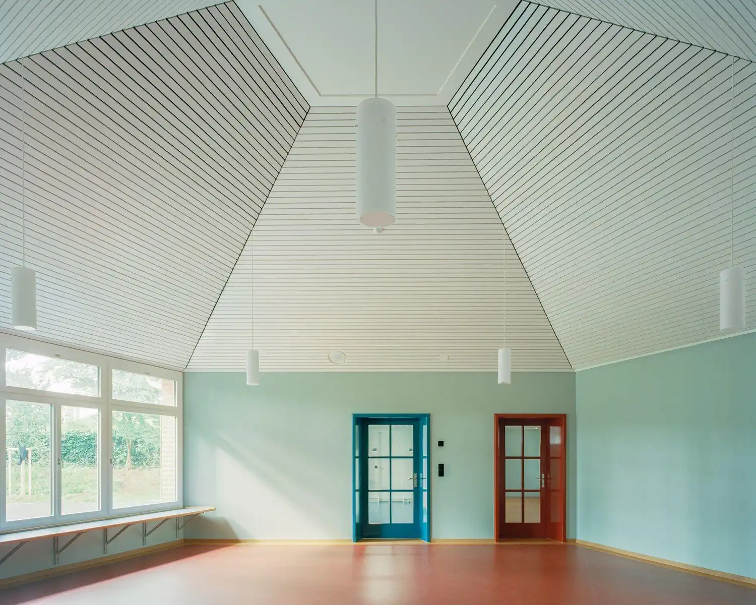 Pentagonal kindergarten room with a white slatted ceiling and red flooring.