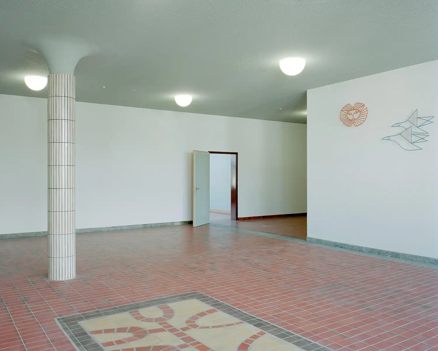 Minimalist school lobby in Switzerland with pink clinker tiles and white tiled columns.