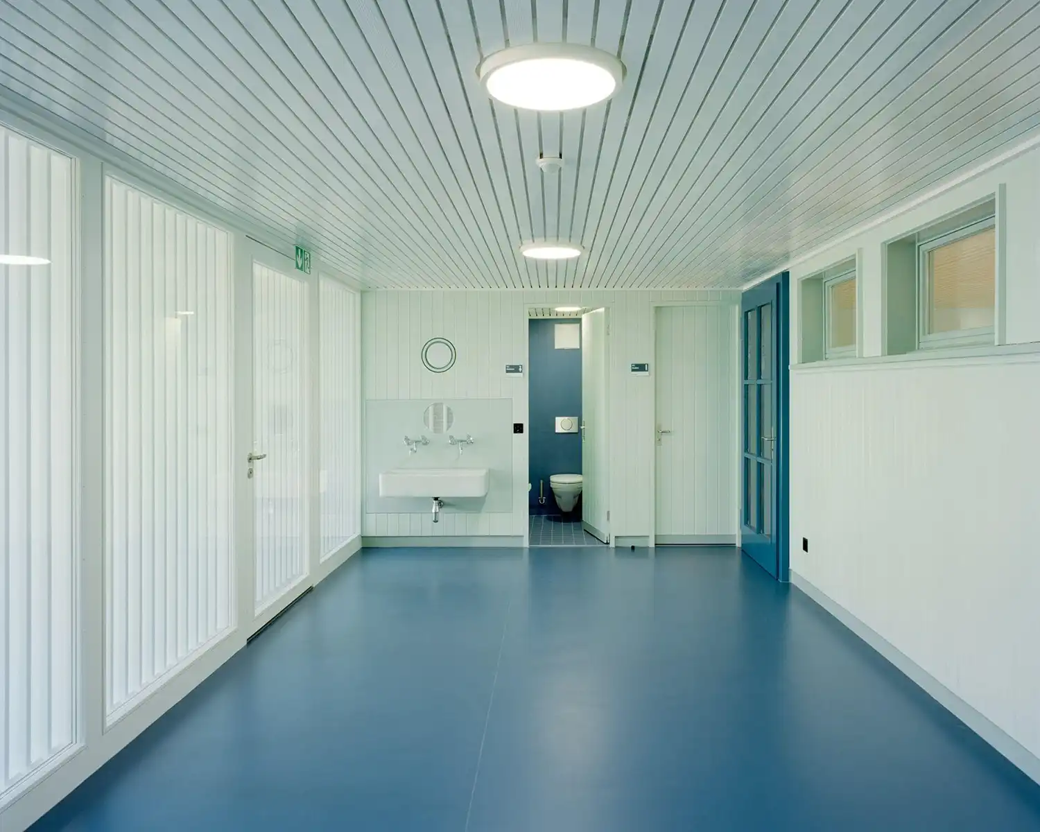Modern school washroom area with blue linoleum and white ribbed wall paneling.