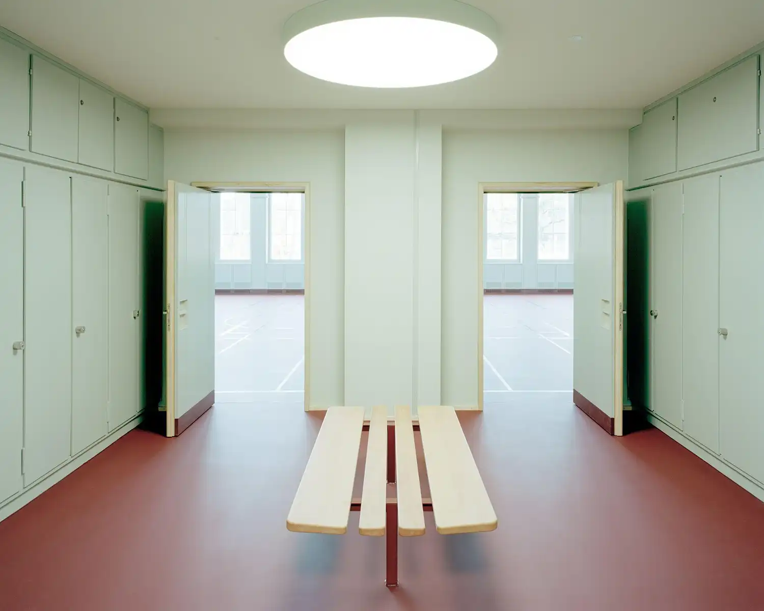 Symmetrical school changing room with red flooring and mint green lockers.