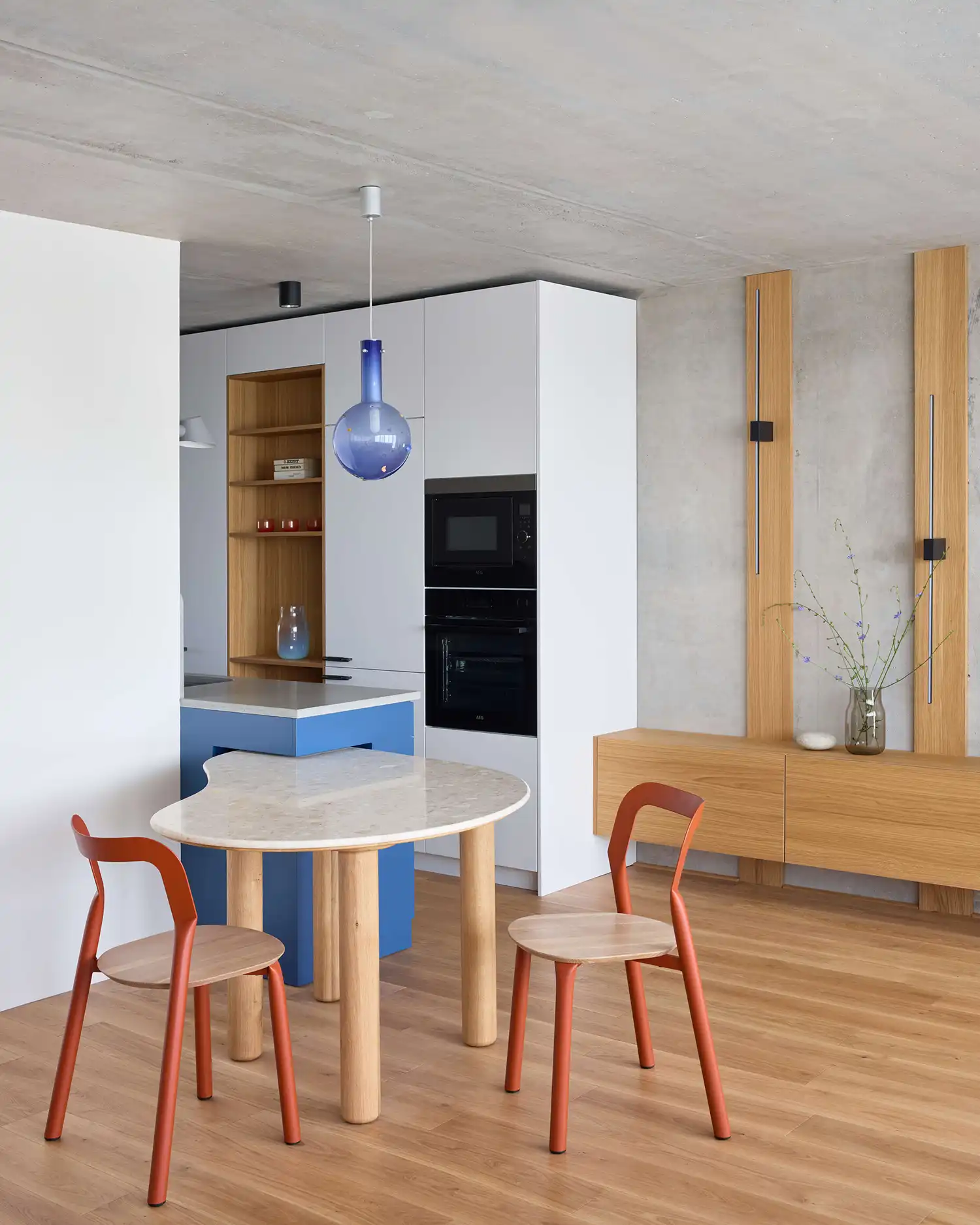 Modern dining area in a Prague renovation featuring a marble-topped table, rust-colored chairs, and a blue glass pendant light.