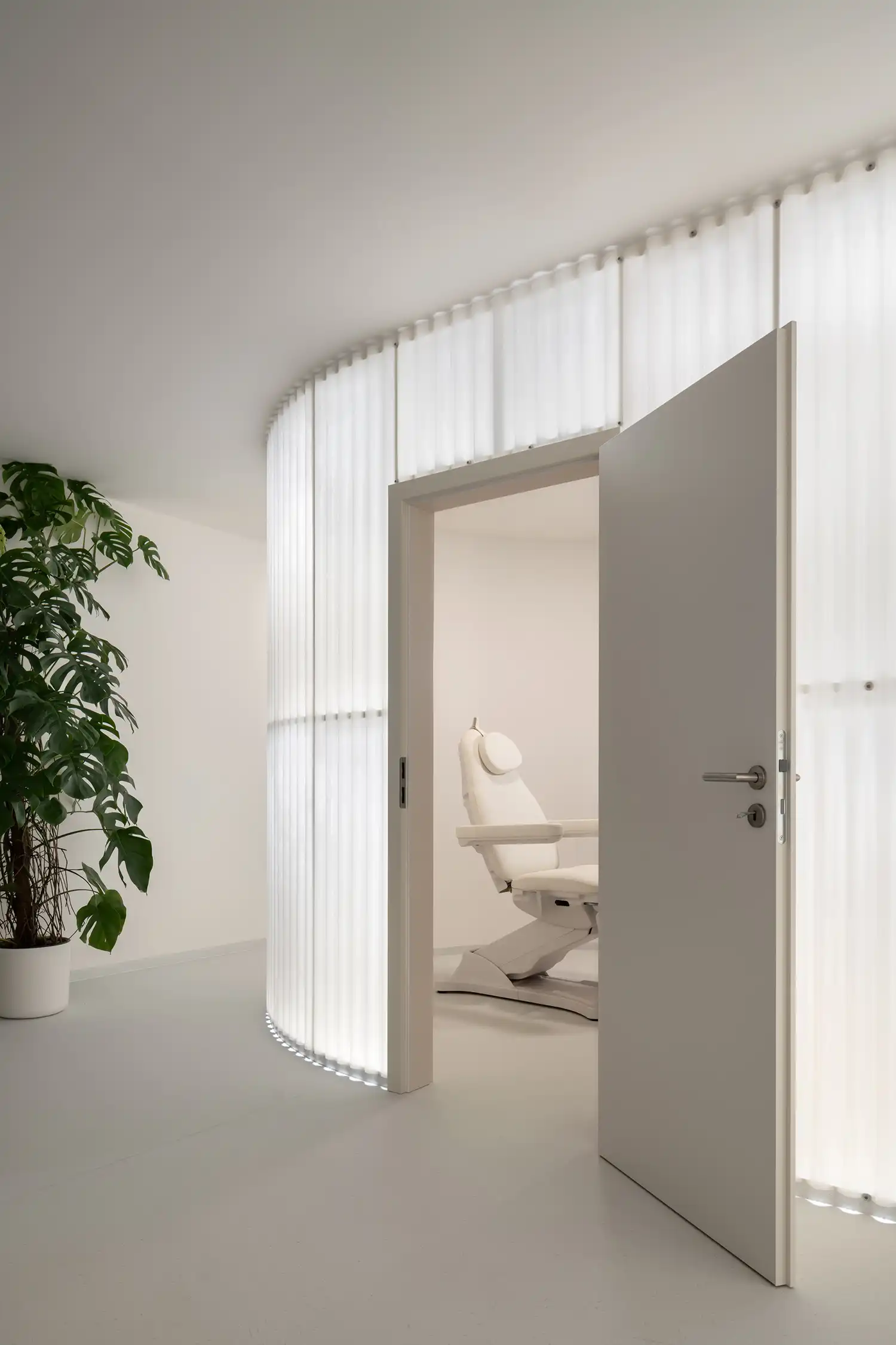 An open door leads into a private treatment room enclosed by a sweeping, backlit fiberglass partitio