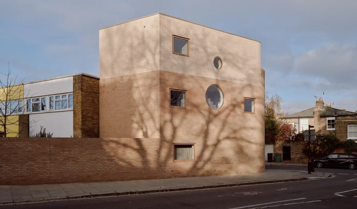 Side-angle view of Runda house in London, showing dual-tone brickwork and a curved corner under a blue sky.