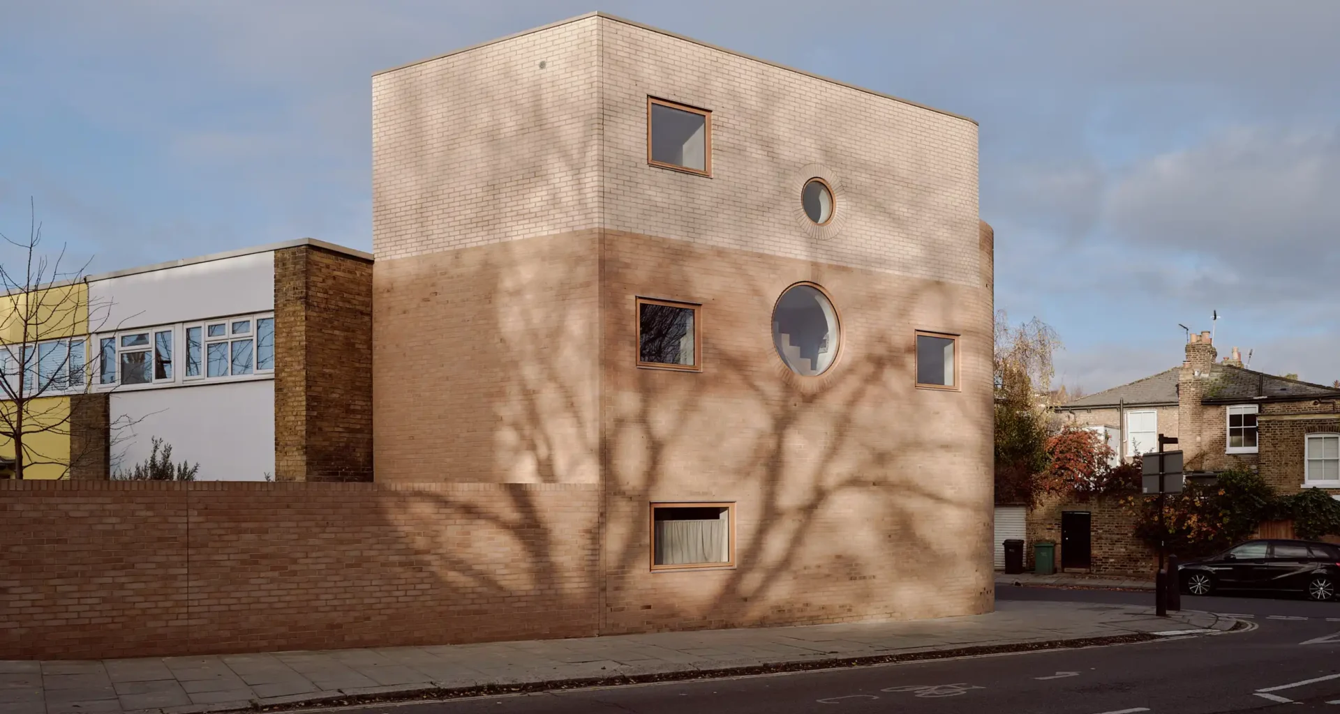 Side-angle view of Runda house in London, showing dual-tone brickwork and a curved corner under a blue sky.