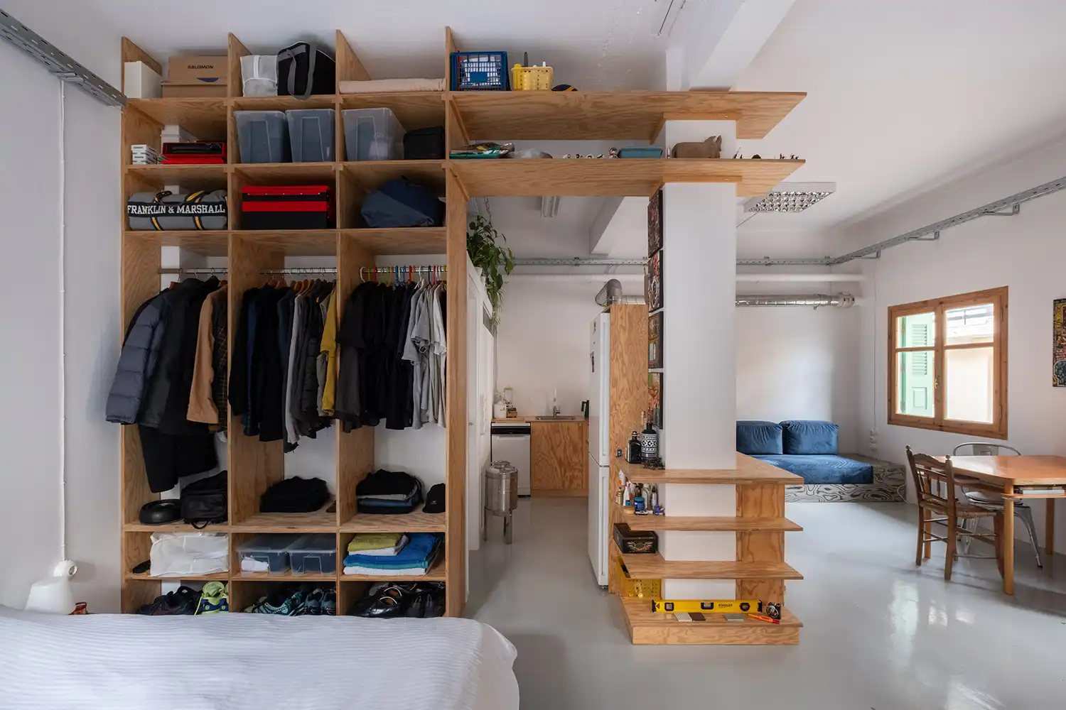 Floor-to-ceiling pine plywood wardrobe and storage unit dividing the bedroom and living areas.