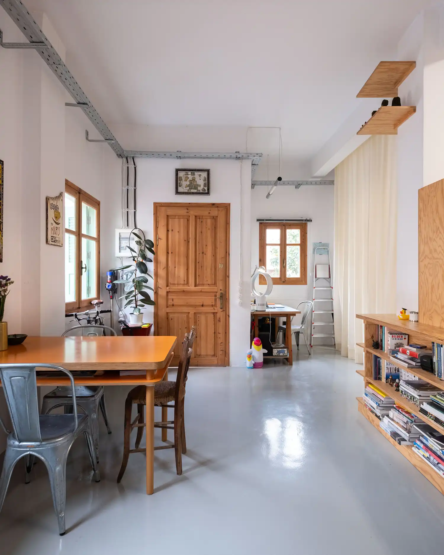 View of the studio entrance featuring a wooden door, industrial cable trays, and a minimalist work desk.