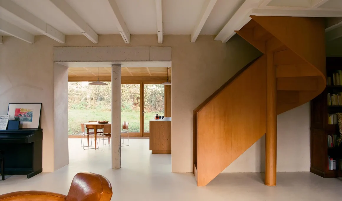 Interior of Plouër-sur-Rance House showing circular concrete column and wooden staircase.