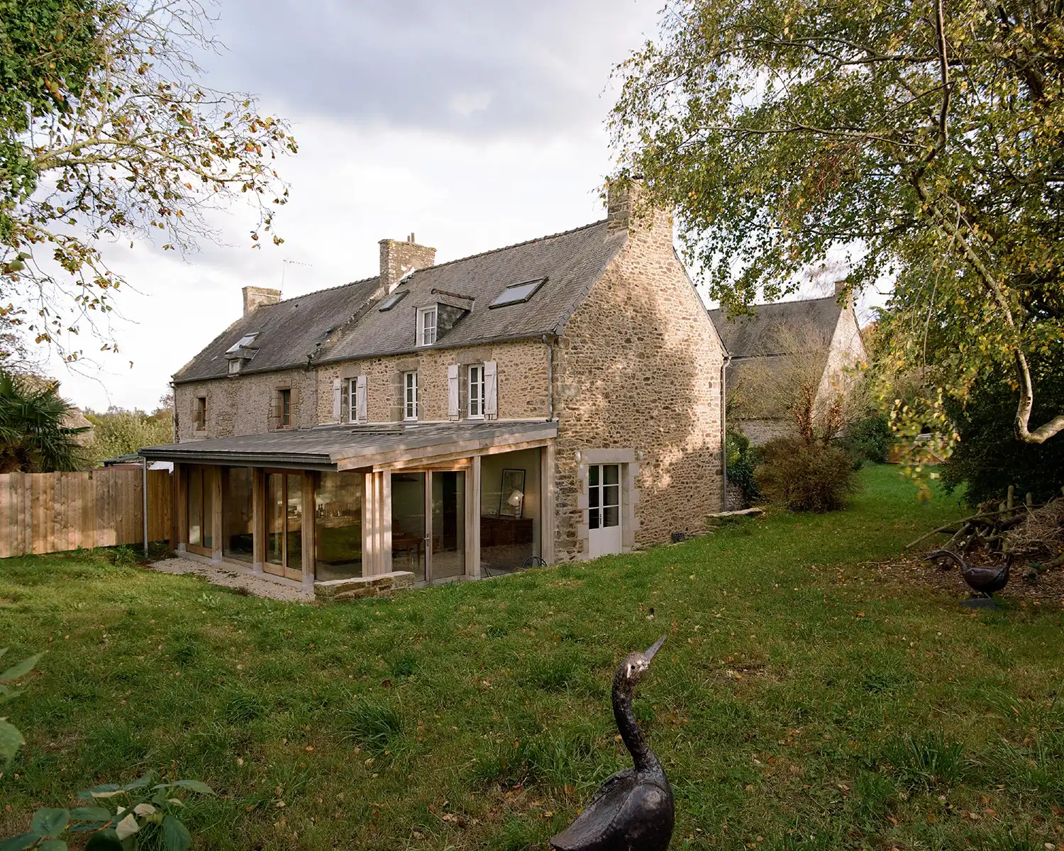Exterior of a traditional stone house in Brittany with a modern glass and wood extension.