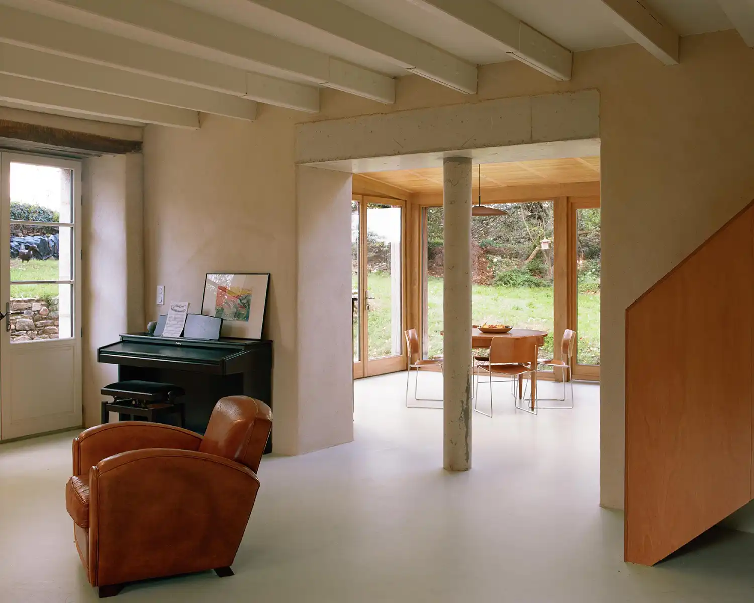 Modern living room with a concrete threshold looking toward a dining area and garden.