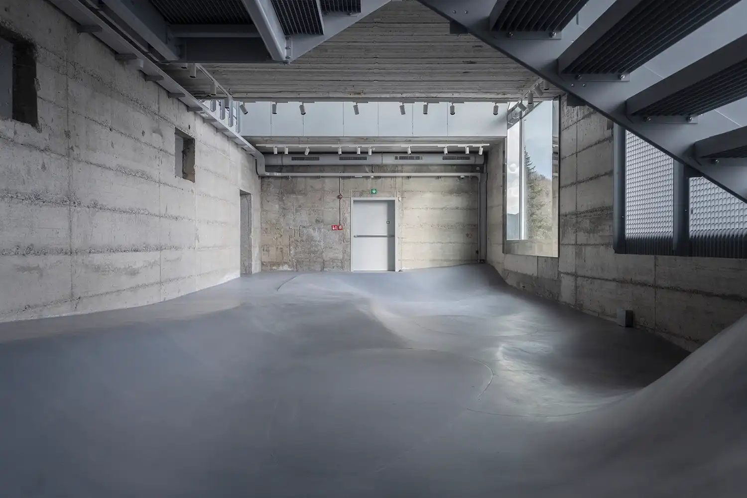 Minimalist interior with undulating grey floor and raw concrete walls in the Reinhold Messner Haus.