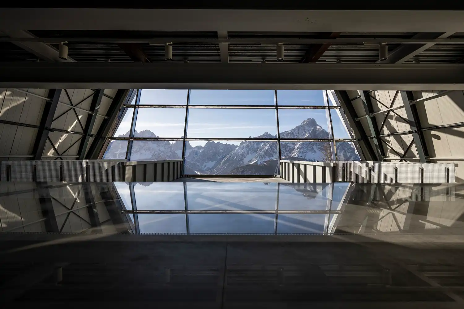 Dramatic interior view of the main hall at Reinhold Messner Haus with a large glass façade framing snowy peaks.