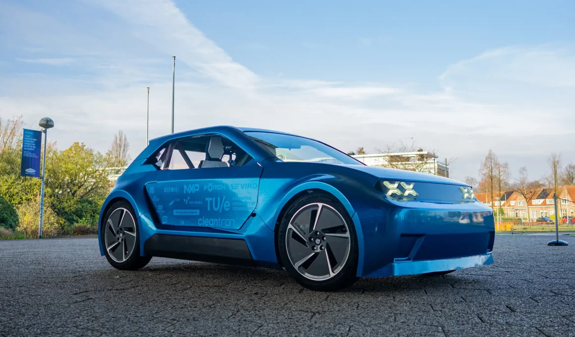 Side profile of ARIA, a blue metallic modular electric car by TU/ecomotive, showcasing sponsor logos on the door.