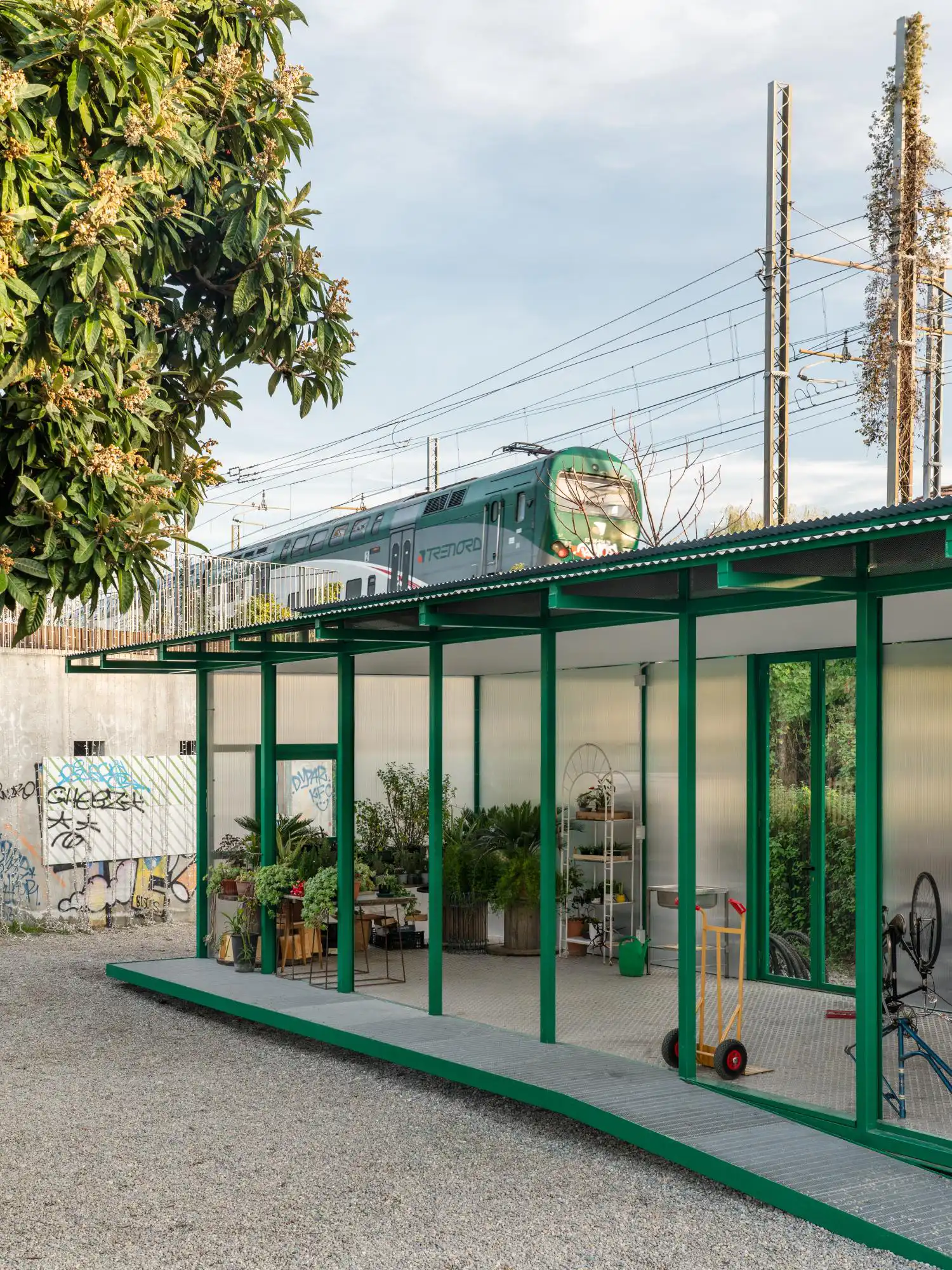 The green pavilion in Milan with a Trenord train passing on the elevated tracks behind it.