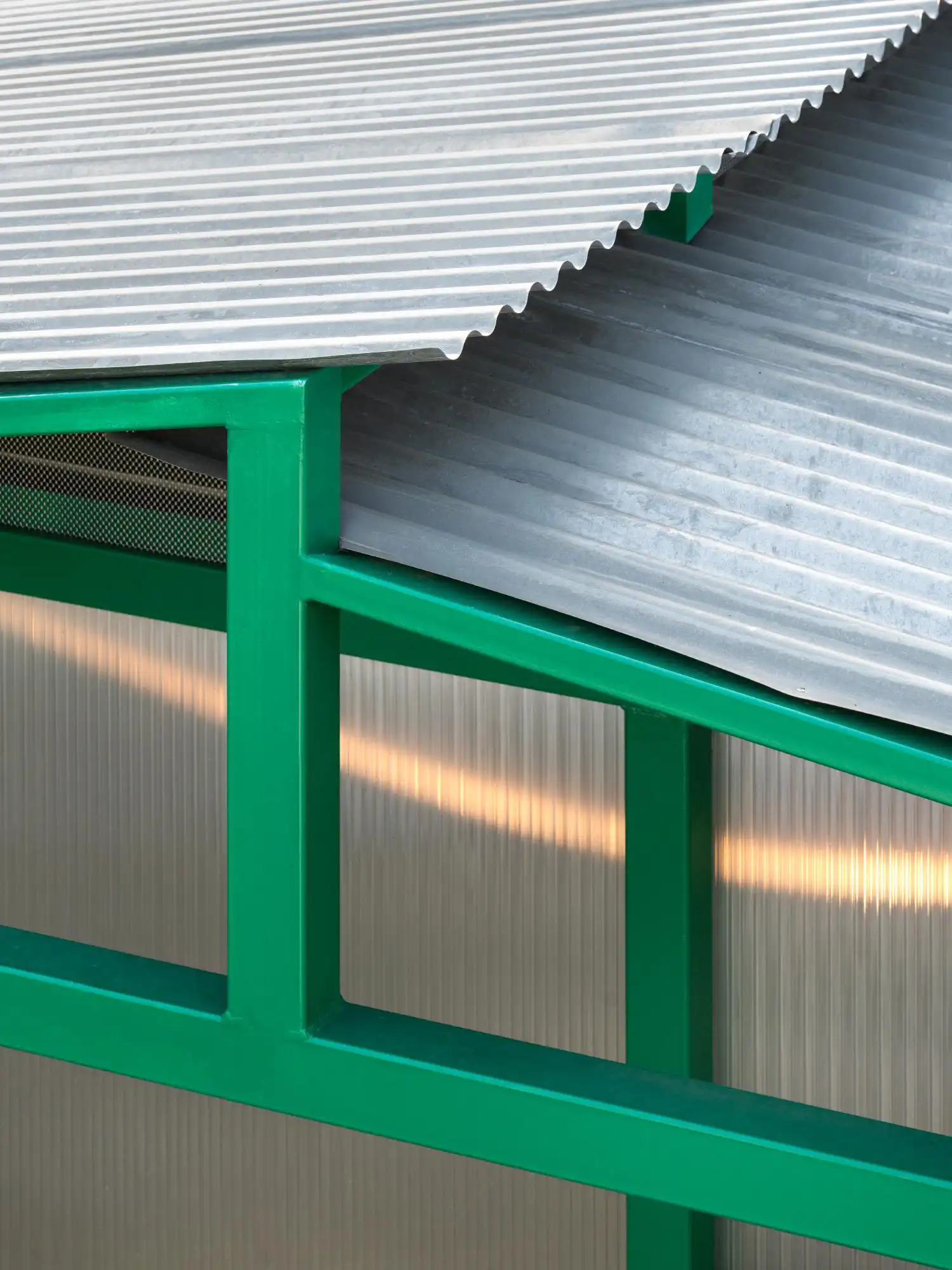 Close-up of the corrugated metal roof and the green steel junction of the San Cristoforo Ciclofficina.