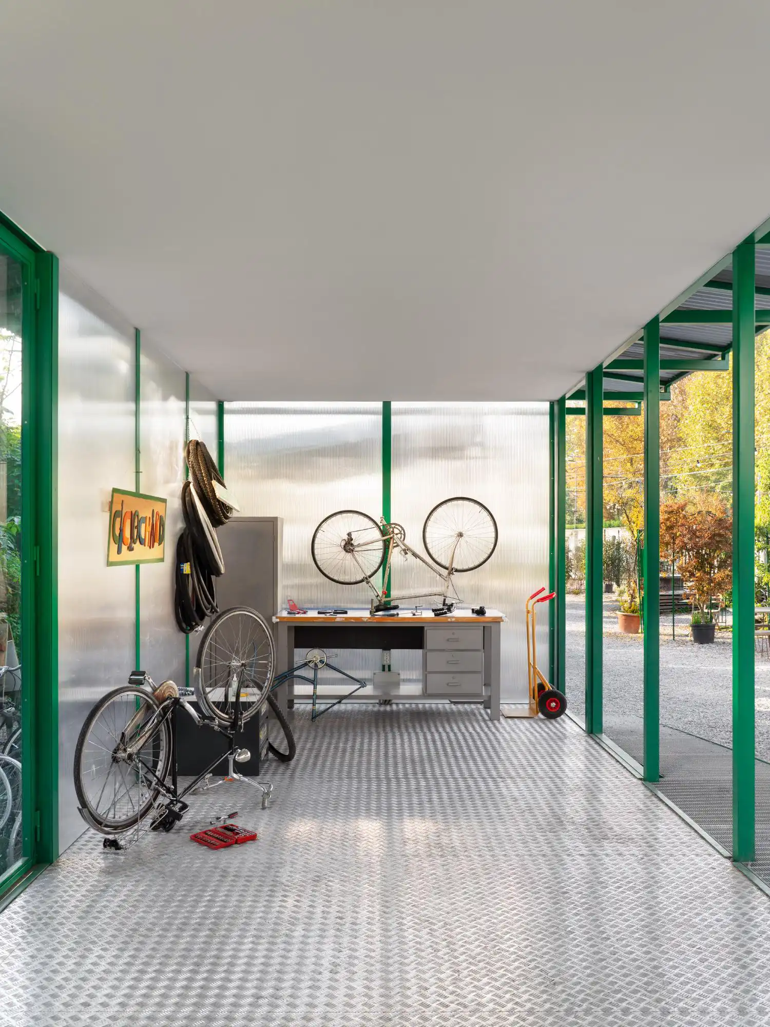 Interior view of the cycle workshop featuring a metal workbench, bicycle tools, and a diamond-plate floor.