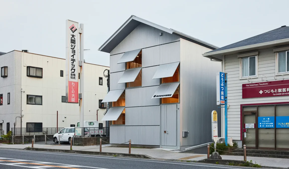 A three-story industrial-chic head office in Fujisawa featuring a silver corrugated metal façade with rhythmic open awning windows and warm timber interiors by Schemata Architects.