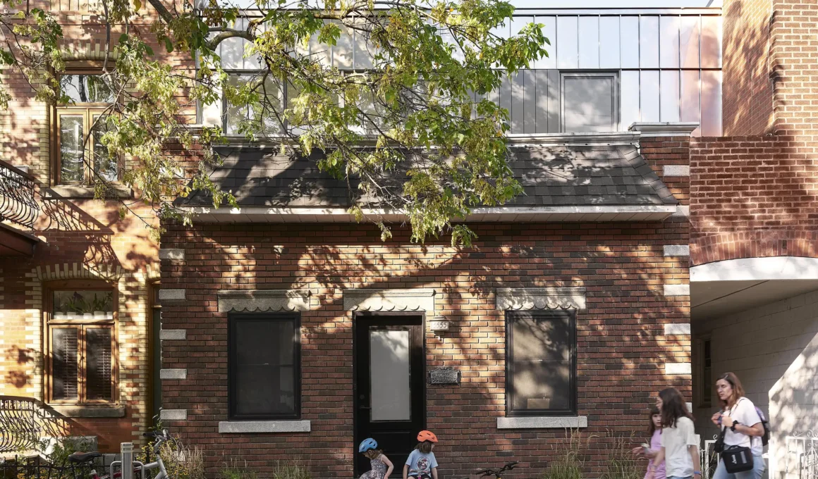 The original brick facade of a traditional Montreal shoebox house with a contemporary recessed stainless steel addition by Alexandre Bernier Architecte.