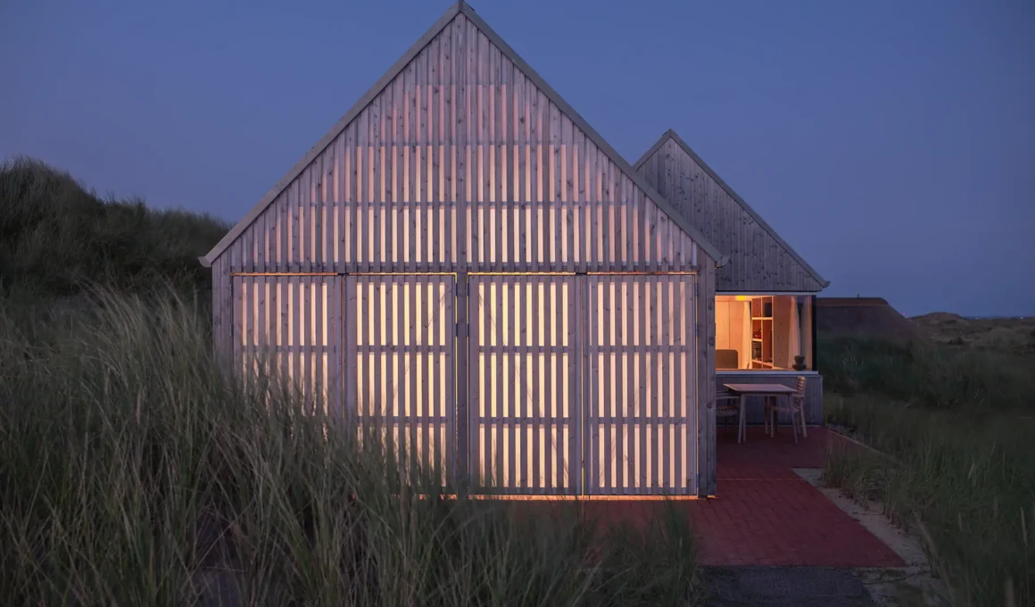 A timber summer house in Klegod at dusk, glowing like a soft lantern through translucent screens.