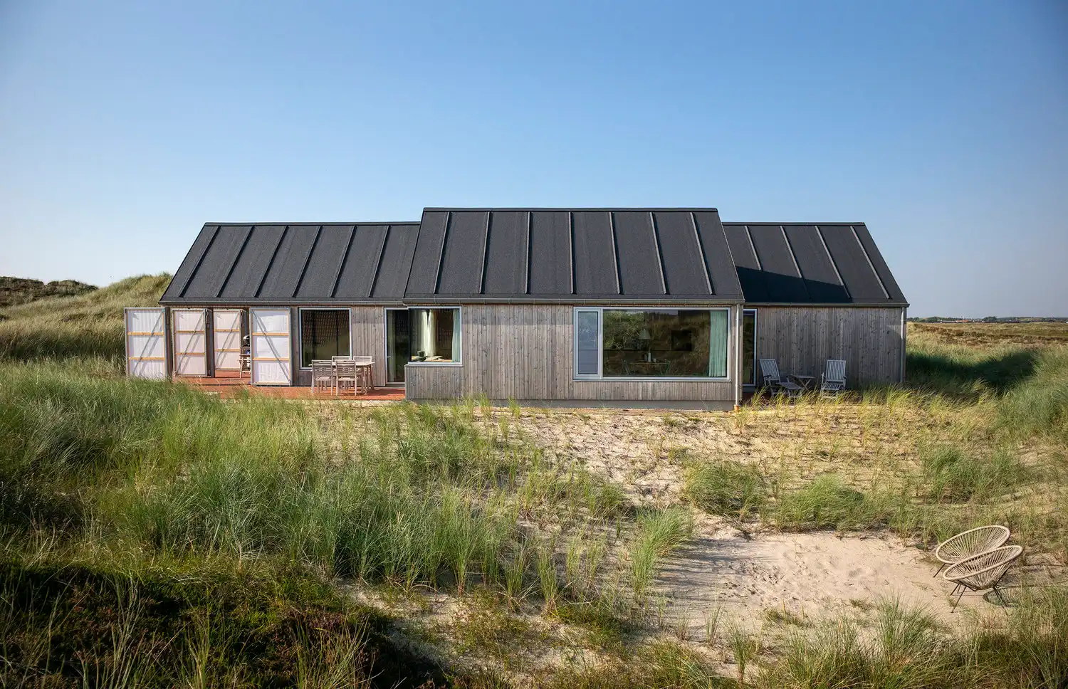 A wide exterior view of the Klegod Summer House by spant studio nestled within high coastal grass.